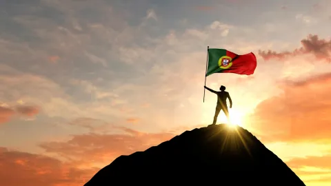 Мужчина держит флаг Португалии на вершины горы